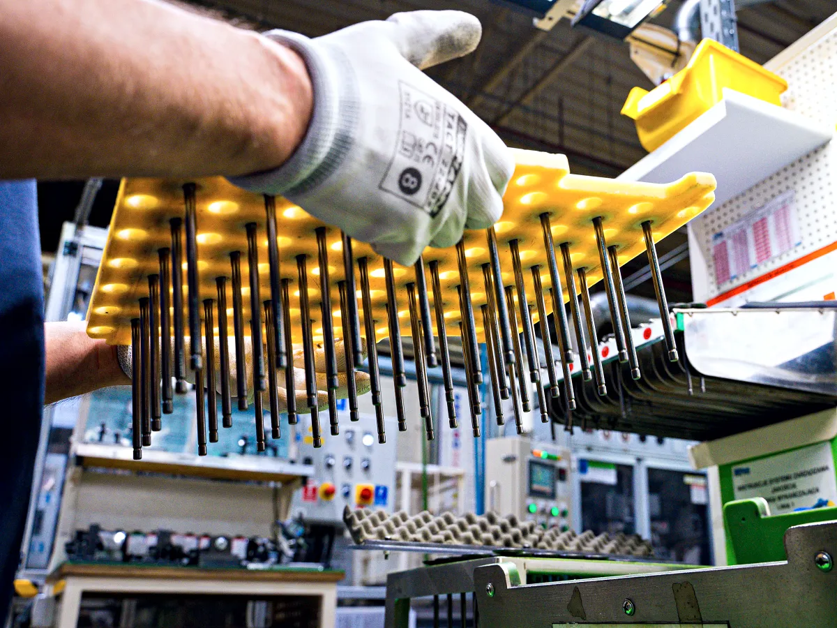 Operator lifting a tray of freshly machined valve stems at the NGV line